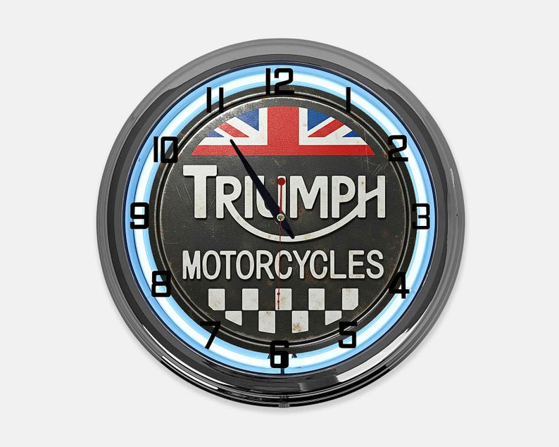 Może przedstawiać: Okrągły zegar Triumph Motorcycles z czarną tarczą, flagą Union Jack i niebieskim neonem. Tarcza zegara zawiera logo Triumph i napis "MOTORCYCLES". Zegar ma chromowaną ramkę.