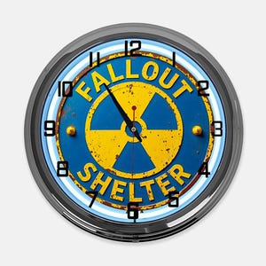 May include: A round wall clock with a blue and yellow Fallout Shelter design. The clock face features a radiation symbol and the words "FALLOUT SHELTER". The clock has a silver-colored metal frame and black hands.