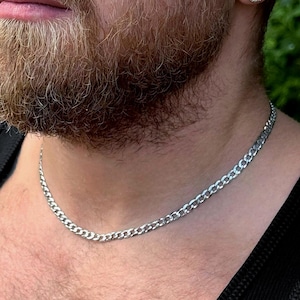 May include: A silver curb chain necklace is worn over a black ribbed vest. The image also shows a man's face and part of his chest. A diamond stud earring is visible in his ear. The brand name "OZCAL" is in the bottom right corner.