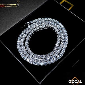 May include: A dazzling silver necklace, featuring multiple strands of clear, round gemstones. The necklace is presented in a black box, enhancing its sparkle. The brand name "OZCAL" is displayed in the bottom right corner.