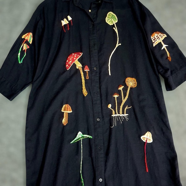 May include: Black button-down shirt with embroidered mushroom designs in various colors. The mushrooms are in shades of red, orange, green, and brown. The shirt has short sleeves and a collared neckline.