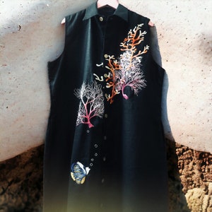 May include: A black sleeveless shirt with a button-up front and embroidered coral designs. A small embroidered fish is near the bottom of the shirt.