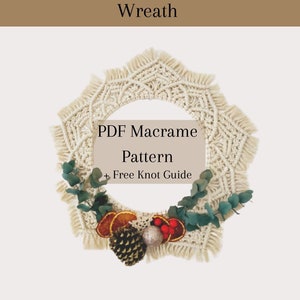 Puede incluir: Una corona de Navidad de macramé blanca decorada con vegetación, naranjas secas y piñas. La corona está adornada con un cartel que dice "Patrón de macramé PDF + Guía de nudos gratuita".