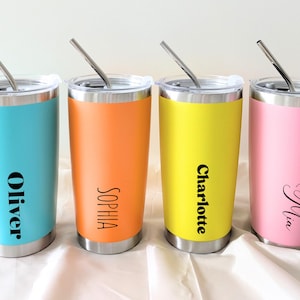 Puede incluir: Cuatro vasos de acero inoxidable con tapas y pajitas. Los vasos son de color azul, naranja, amarillo y rosa. Cada vaso tiene un nombre: Oliver, Sophia, Charlotte y Mia.