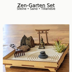 Può includere: Un set da giardino zen in miniatura in un vassoio di legno. Il set include una piccola statua di Buddha, rocce, sabbia, un rastrello e una piccola pianta. Il testo "Zen-Garten Set" è nella parte superiore dell'immagine.