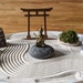 May include: A miniature zen garden with a wooden torii gate, a small golden Buddha statue, a pile of gray stones, a patch of green moss, and a rake on a white plate with white sand.