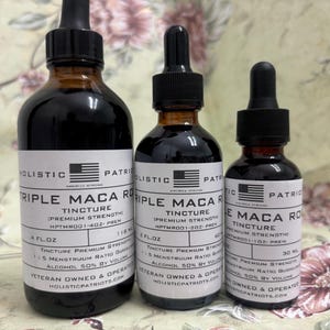 May include: Three glass bottles of Triple Maca Root Tincture, labeled "Holistic Patriots", with a red, white, and blue American flag logo. The bottles are filled with a dark brown liquid and have black dropper caps. The labels state "Premium Strength" and "Veteran Owned & Operated".