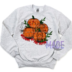 May include: A grey sweatshirt featuring a design of three orange pumpkins with spooky faces, a spider web, and the text "Welcome to the Patch".