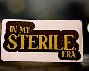 Könnte beinhalten: Ein weißer Aufkleber mit schwarzen und goldenen Buchstaben, auf dem "In My Sterile Era" steht.