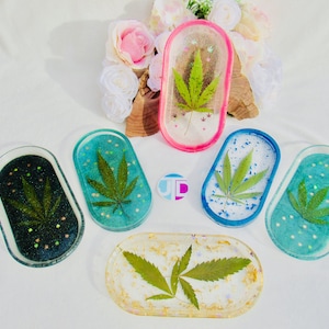 May include: Six oval-shaped resin trays with a clear, glossy finish. Each tray features a pressed green leaf with a white background and colorful flecks. The trays are in various colors, including pink, blue, teal, and gold.