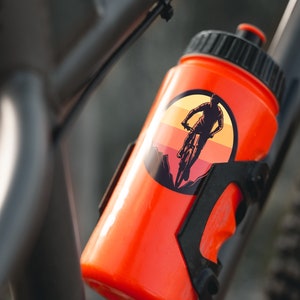 May include: Orange water bottle with a black cap and a sticker of a person riding a mountain bike in a sunset scene.