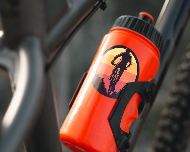May include: Orange water bottle with a black cap and a sticker of a person riding a mountain bike in a sunset scene.