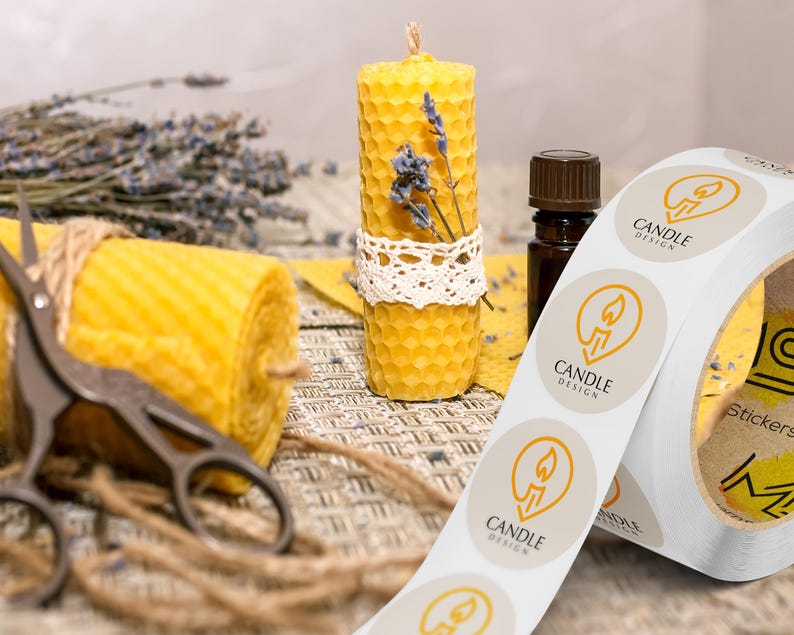 Custom sticker labels displayed on a roll beside beeswax candles, scissors, dried florals, and twine on a neutral tabletop, showing round logo stickers in roll format.