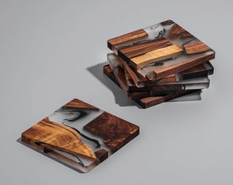 May include: A stack of square coasters made of wood and clear resin. The wood pieces are various shades of brown and tan, while the resin has a marbled, smoky appearance. One coaster is separate from the stack, lying flat.