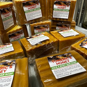 Könnte beinhalten: Mehrere Stück Seife für Gesicht und Körper mit Kurkuma und Honig, verpackt in Plastik. Die Seife ist leuchtend orangefarben und trägt ein Etikett mit der Aufschrift "Turmeric & Honey Face & Body Bar Soap" und "Helps with Acne | Hyperpigmentation".