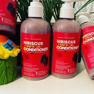 May include: Three bottles of purple hibiscus leave-in conditioner with a white pump top. The bottles have a red label with white text that reads "RHO TREASURE HIBISCUS Leave in CONDITIONER".