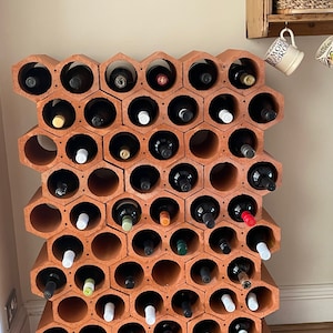 May include: A terracotta wine rack with a hexagonal design holds multiple bottles of wine. The rack is made of clay and has a rustic look.