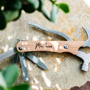 Könnte beinhalten: Ein Multitool mit einem Holzgriff, der mit dem Namen "Matthias" graviert ist. Das Werkzeug verfügt über einen Hammer, einen Nagelzieher, eine Säge, eine Feile und einen Flaschenöffner.
