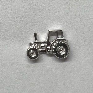 Puede incluir: Un amuleto de plata con forma de tractor. El tractor tiene un diseño detallado con ruedas y una cabina visibles.