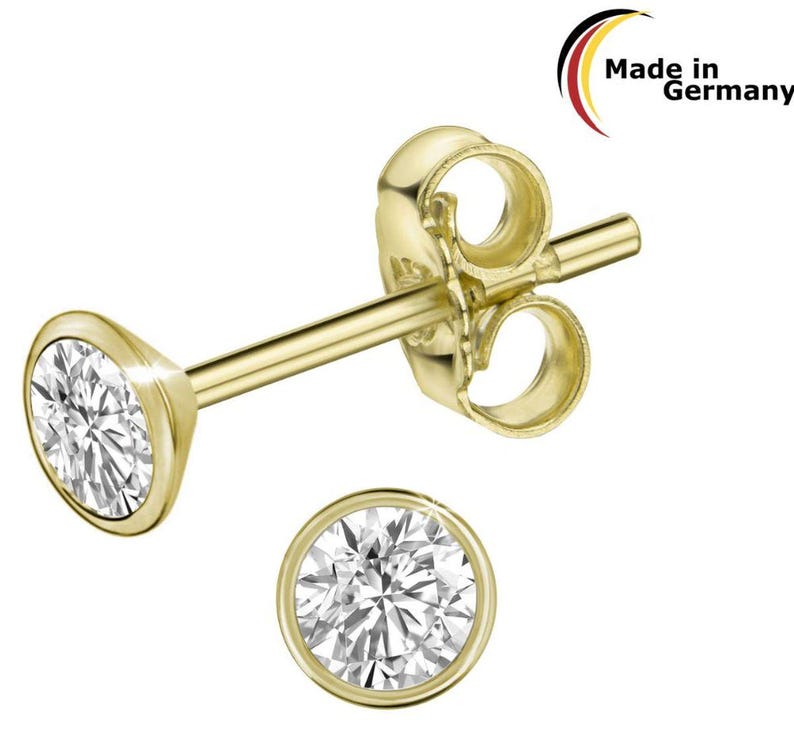 May include: Gold-coloured stud earrings with a round, clear gemstone set in a bezel. The earrings are displayed on a white background. The text "Made in Germany" is visible in the upper right corner.