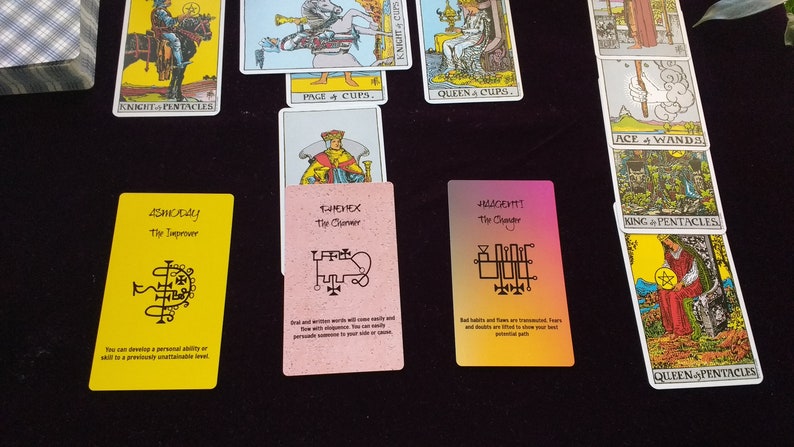 Puede incluir: Una colecci&oacute;n de cartas de tarot dispuestas sobre una superficie oscura, incluyendo cartas tradicionales Rider-Waite como el Caballero de Oros y la Reina de Oros, junto a tres cartas or&aacute;culo modernas en tonos amarillo, rosa y un degradado naranja-morado.