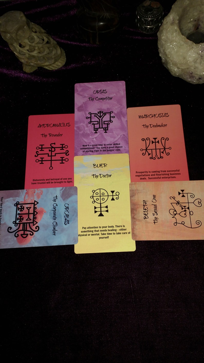 Puede incluir: Un conjunto de cinco cartas de or&aacute;culo rectangulares dispuestas en forma de cruz. Las cartas presentan fondos coloridos, sellos negros y texto que incluye nombres como Andromalius, Orias, Marchosias, Buer, Orobas y Beleth con sus t&iacute;tulos.