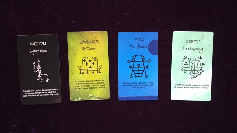 Puede incluir: Cuatro cartas de or&aacute;culo rectangulares dispuestas horizontalmente. La primera es negra con texto blanco Pazuzu, la segunda amarilla con Barbatos, la tercera azul con Ipos y la cuarta verde claro con Berith. Cada carta presenta un sello negro &uacute;nico.