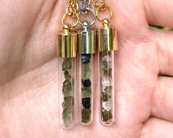 May include: Three gold-toned necklaces with glass vials filled with green and clear crystals. The vials are attached to gold-toned chains.