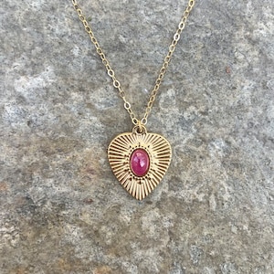 May include: A gold chain necklace with a heart-shaped pendant featuring a pink gemstone in the center.