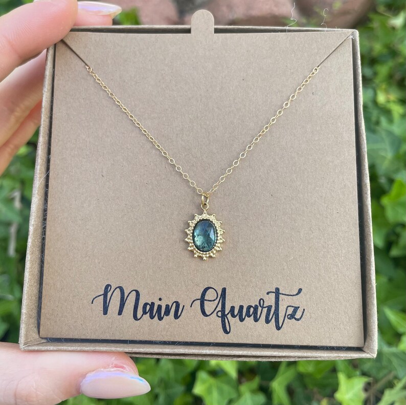 May include: A gold necklace with a green gemstone pendant in a sunburst setting. The pendant is labeled "Main Quartz".