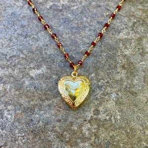 May include: A gold heart-shaped locket necklace with a delicate chain and red gemstone beads.