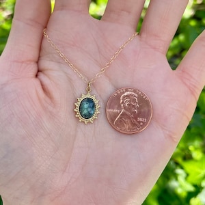 May include: A gold chain necklace with a green gemstone pendant set in a gold sunburst design. The pendant is about the size of a US penny.