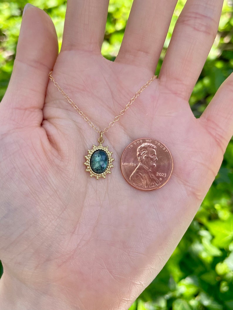 May include: A gold chain necklace with a green gemstone pendant set in a gold sunburst design. The pendant is about the size of a US penny.