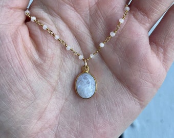 May include: A delicate gold chain necklace with a white moonstone pendant. The chain is made of small, round beads.