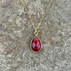 May include: A gold chain necklace with a teardrop-shaped pendant featuring a deep red gemstone.