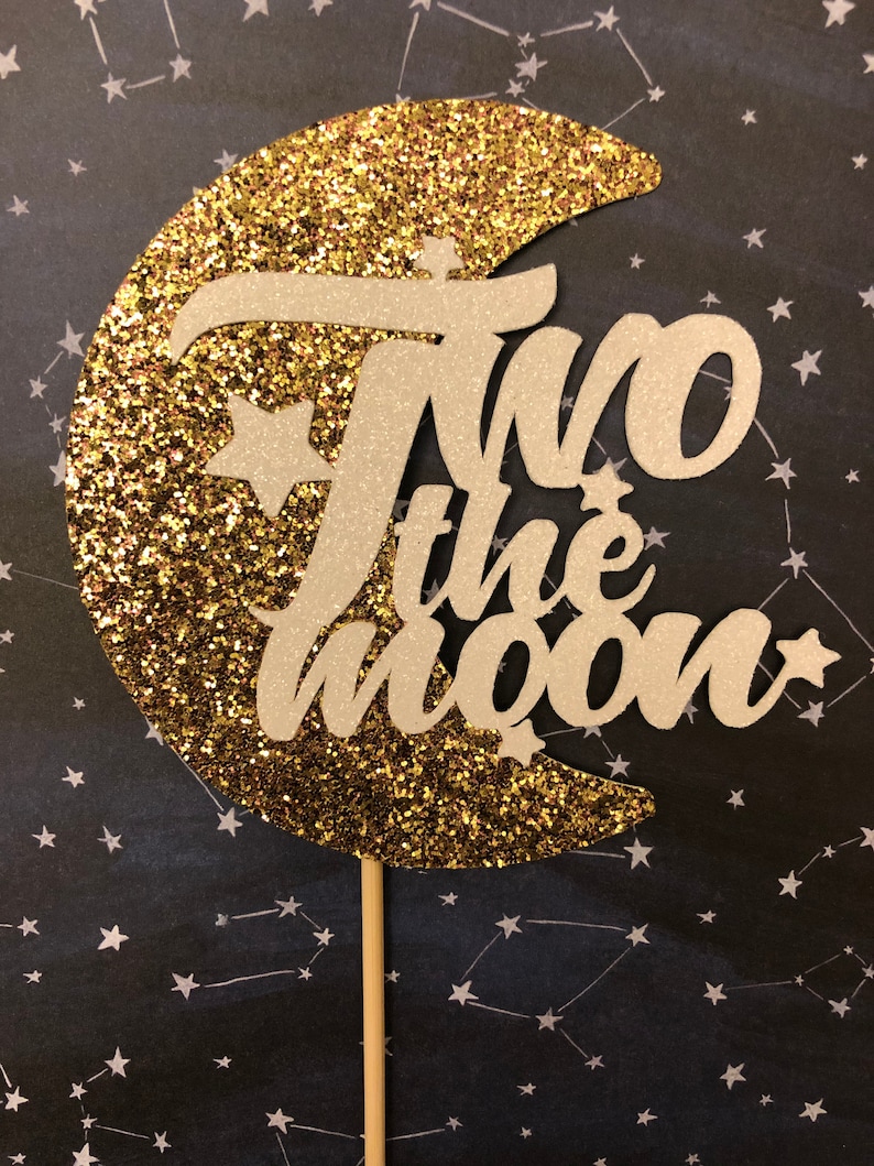 May include: Gold glitter moon cake topper with white lettering that says "Two the Moon" and a small star on each side.