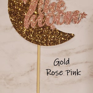 May include: Gold glitter crescent moon cake topper with the words "Two the Moon" in rose pink glitter.