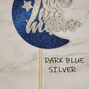 May include: A blue and silver glitter moon cake topper with the text "Two the Moon" and two stars.
