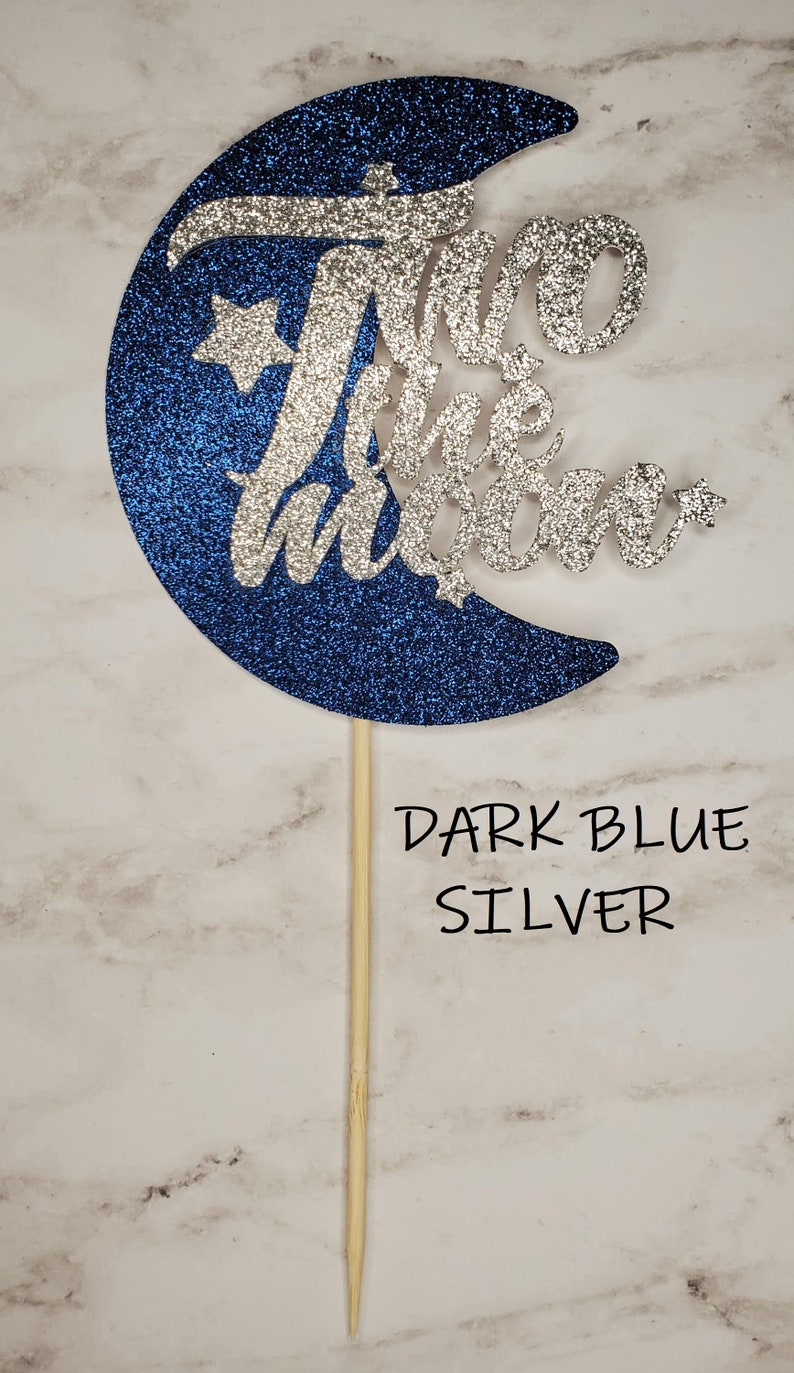 May include: A blue and silver glitter moon cake topper with the text "Two the Moon" and two stars.