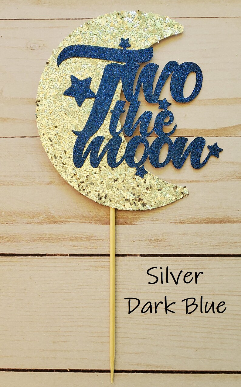 May include: A gold glitter crescent moon with a dark blue glitter "Two the Moon" cake topper.