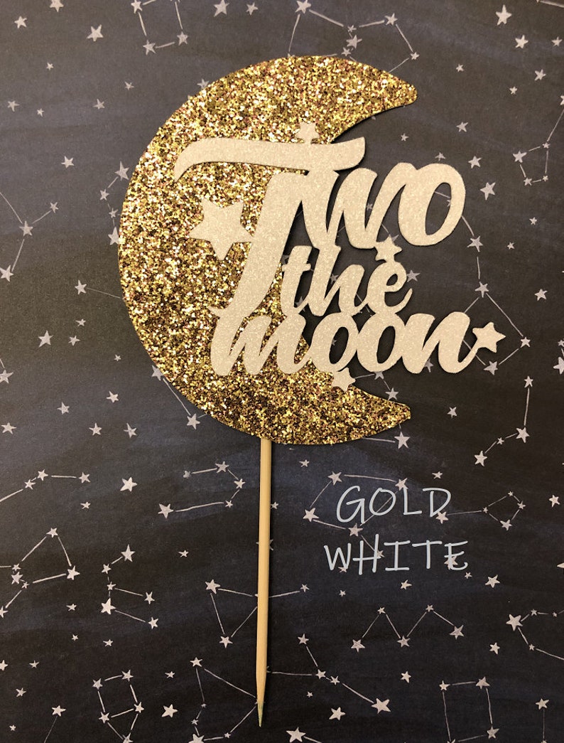May include: Gold glitter moon cake topper with the words "Two the Moon" in white. The topper is on a black background with white stars.