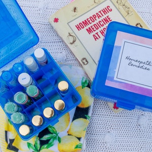 May include: A blue plastic case with a label that says "Homeopathic Remedies" and a smaller blue case filled with small glass bottles. The smaller case is sitting on a white and yellow patterned towel.