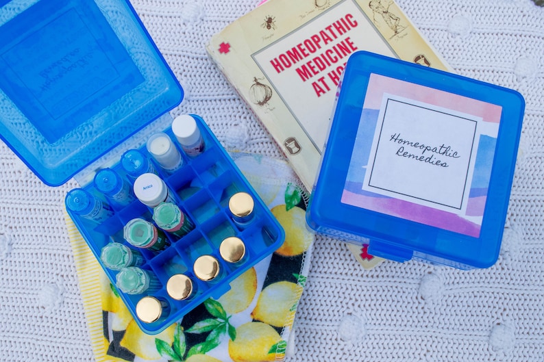 May include: A blue plastic case with a label that says "Homeopathic Remedies" and a smaller blue case filled with small glass bottles. The smaller case is sitting on a white and yellow patterned towel.