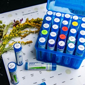 May include: A blue plastic case filled with small blue vials, some with colored labels. A bundle of dried herbs and a sheet of paper with printed text are also present. One vial reads "30".