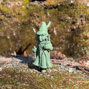 Puede incluir: Una figurita verde impresa en 3D de un personaje de fantasía que lleva un sombrero puntiagudo y sostiene un bastón. El personaje tiene orejas grandes y una túnica larga.