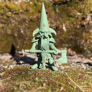 Puede incluir: Una figurita de plástico verde de un gnomo que lleva un sombrero puntiagudo con diseños intrincados y sostiene un hacha. El gnomo tiene una barba larga y lleva armadura.