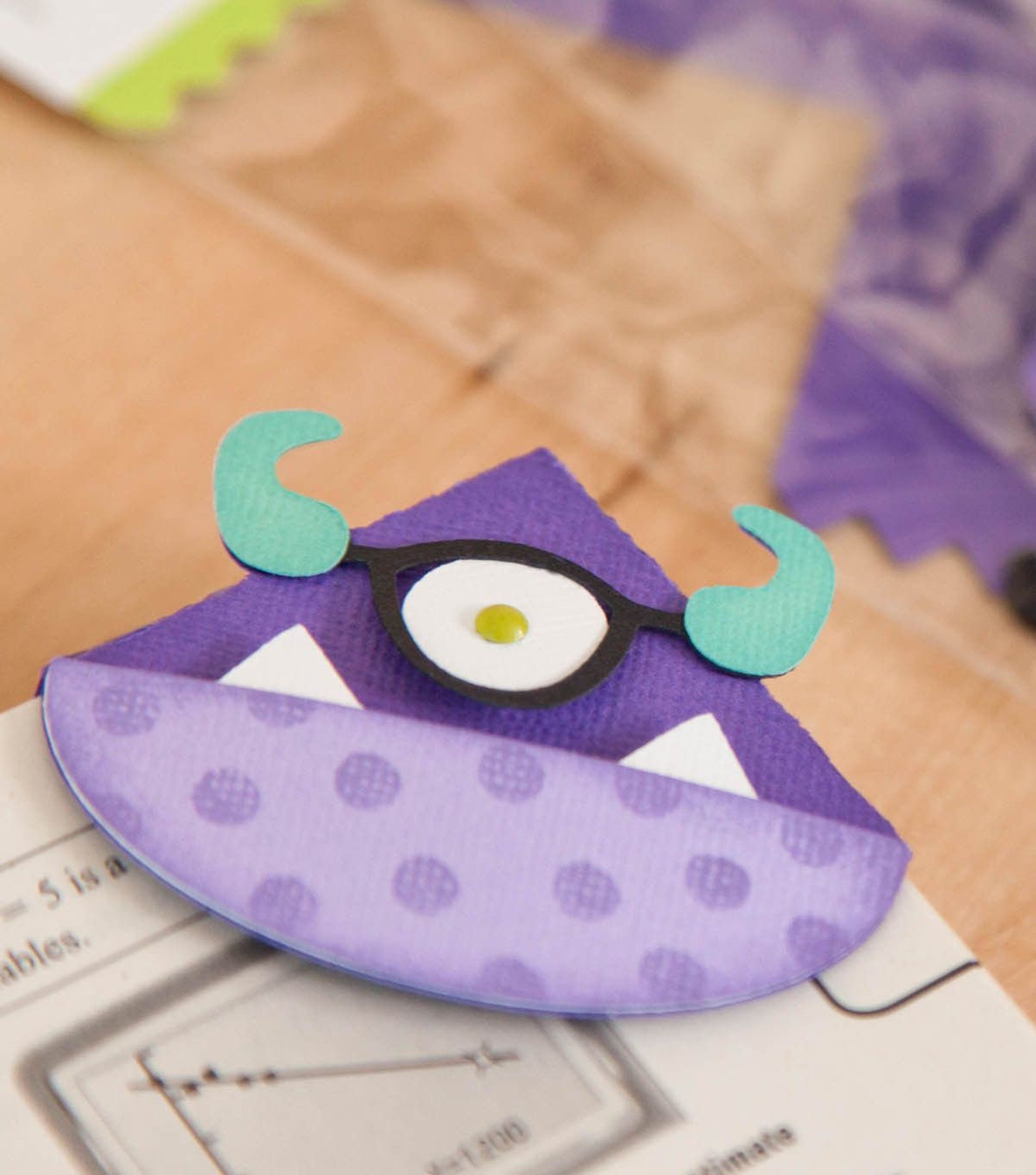 A purple monster bookmark with one eye and horns attached to the corner of an open book