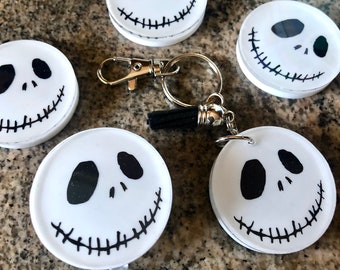 May include: Four white round badge reels featuring a black and white Jack Skellington face design. The reels are attached to a silver key chain with a black tassel.