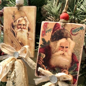 May include: Two vintage Christmas ornaments featuring images of Santa Claus. Each ornament is made of wood and has a fabric bow with a sparkly embellishment. The ornaments are hung with twine and have a white and red bead at the top.