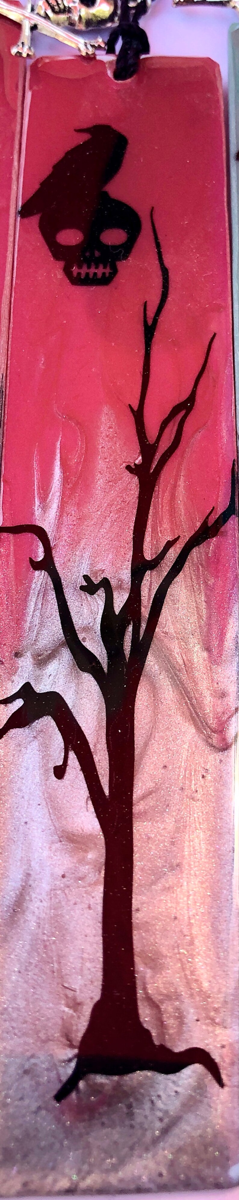 May include: A black crow with a skull head sits above a black silhouette of a bare tree on a pink and white background.